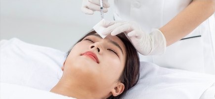 시술 베드에 누운 여성의 이마에 주사 시술을 하는 모습