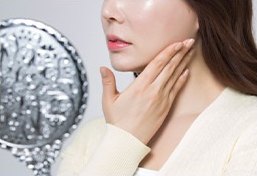 목과 턱을 손으로 감싼 여성과 은빛 화장품 오브제