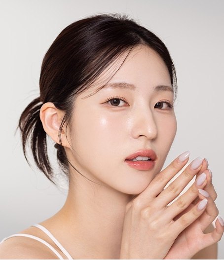 맑은 피부의 여성 모델이 두 손을 턱 옆에 모으고 정면을 바라보는 모습