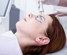 보호 안경을 쓰고 누운 여성의 얼굴에 시술자가 레이저 핸드피스를 대고 있는 모습